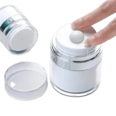 A clear cylindrical cosmetic jar with a white screw-top lid and a small white central button, shown with a hand pressing that button. A separate clear lid and another jar are visible on a plain white background.