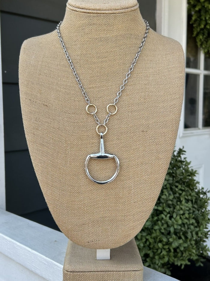 Silver necklace with a unique Snaffle Bit pendant on a beige mannequin bust outdoors.