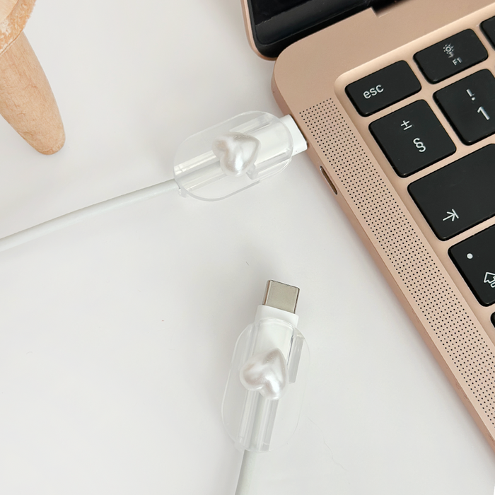 Pearl heart-shaped cable cover charm on a USB-C charging cable next to a rose gold laptop.