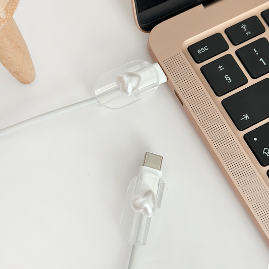 Pearl heart-shaped cable cover charm on a USB-C charging cable next to a rose gold laptop.