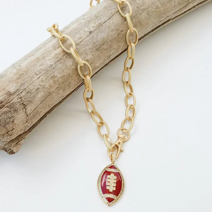 Show your team spirit with this Football Necklace featuring a vibrant colored enamel football pendant on a stylish gold etched chain. Perfect for game day, it adds a spirited touch to any outfit while keeping you ready to cheer on your favorite team in style.

Details:

20" Chain
24k Gold Plated&nbsp;