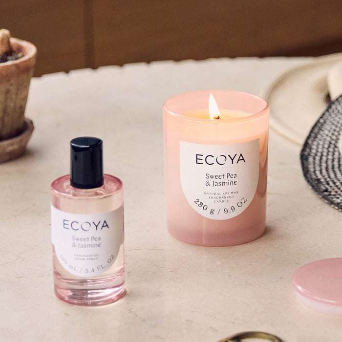 Sweet pea & jasmine candle burning on a table with a room spray and sunhat.
