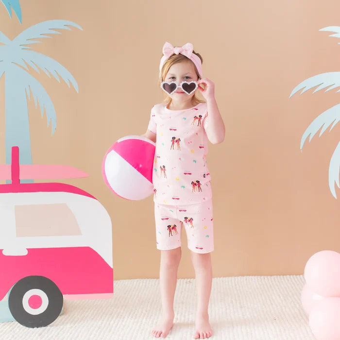 Girl posing in Kyte Baby Barbie™ Beach pajama set with short sleeves, matching shorts, and playful print.