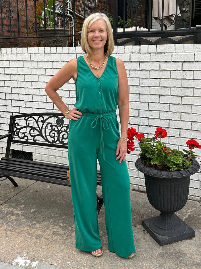 How flattering and cute is this sleeveless knit jumpsuit in rich pine green! The fabric is amazing... a soft, lightweight knit. The jumpsuit features a flattering V-neckline and button-up bodice with an elastic waist and an adjustable tie. Whether you're heading to brunch, running errands, or enjoying a casual evening out, this versatile piece works beautifully on its own or layered under a denim jacket when temperatures drop.&nbsp;

Barbara is wearing a small.&nbsp;

Material: 48% Rayon / 36% Polyester / 1