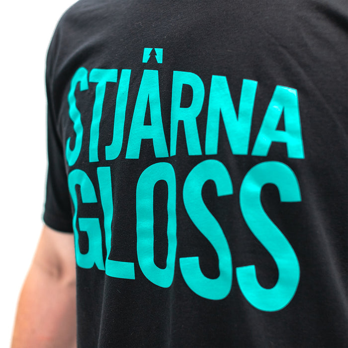 A closeup of the teal words 'Stjarnagloss' on the front of a black t-shirt.